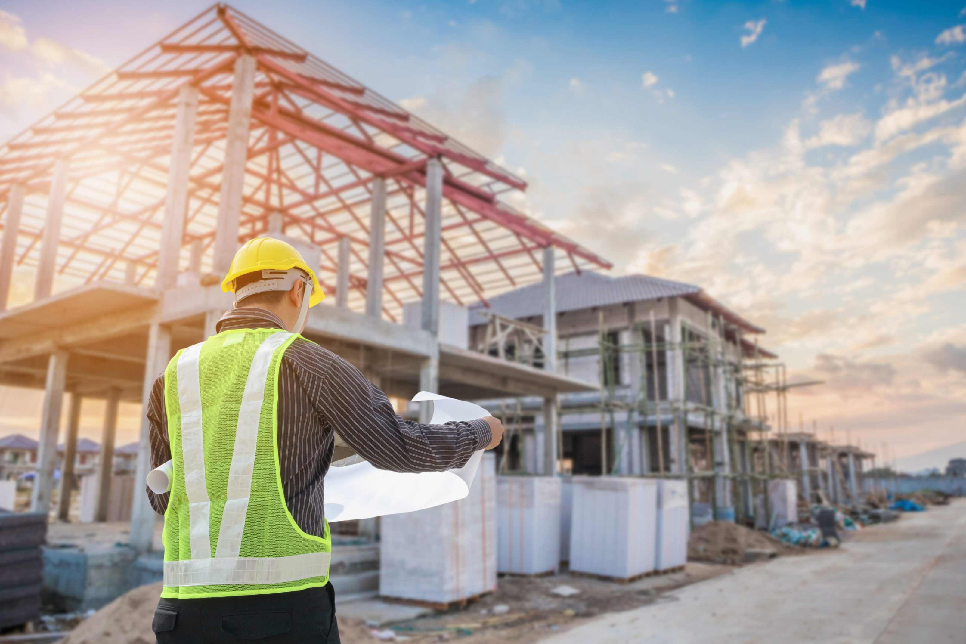 Construction worker examines plans at building site during sunset.