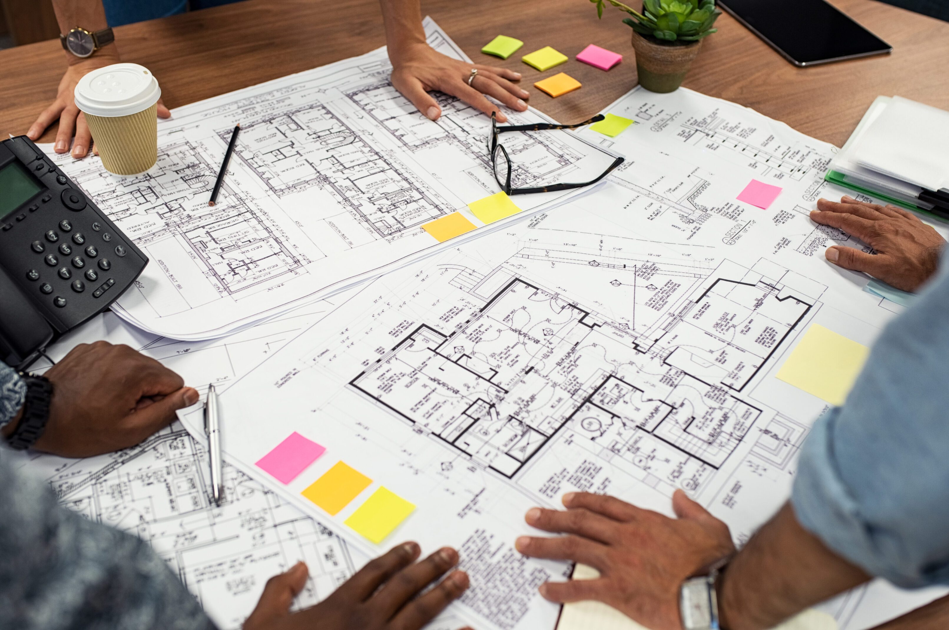 Architects collaborating over building blueprints with colorful sticky notes.