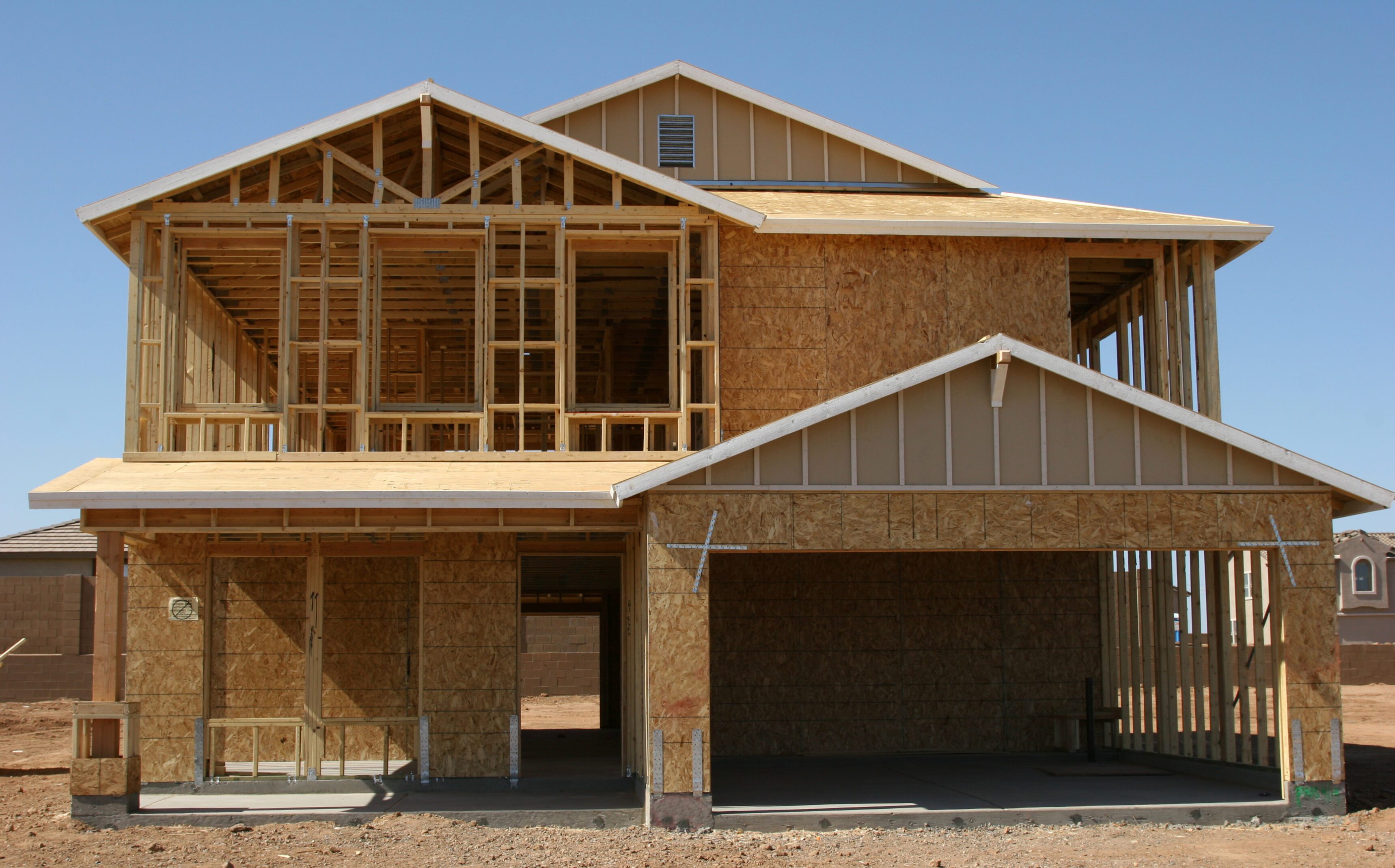 Two-story house under construction with wooden framing and sheathing.