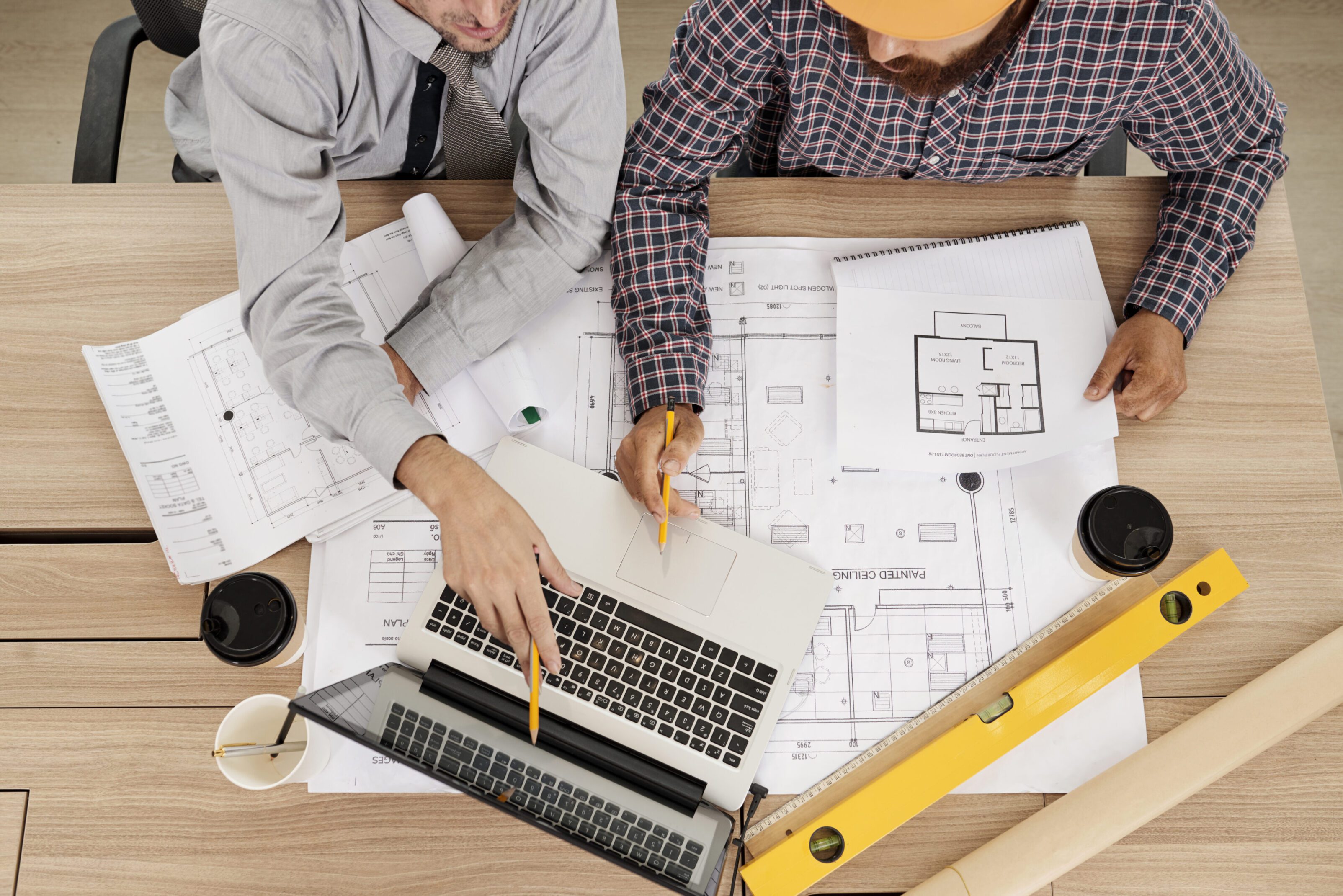 Two professionals discussing architectural blueprints with a laptop and tools.