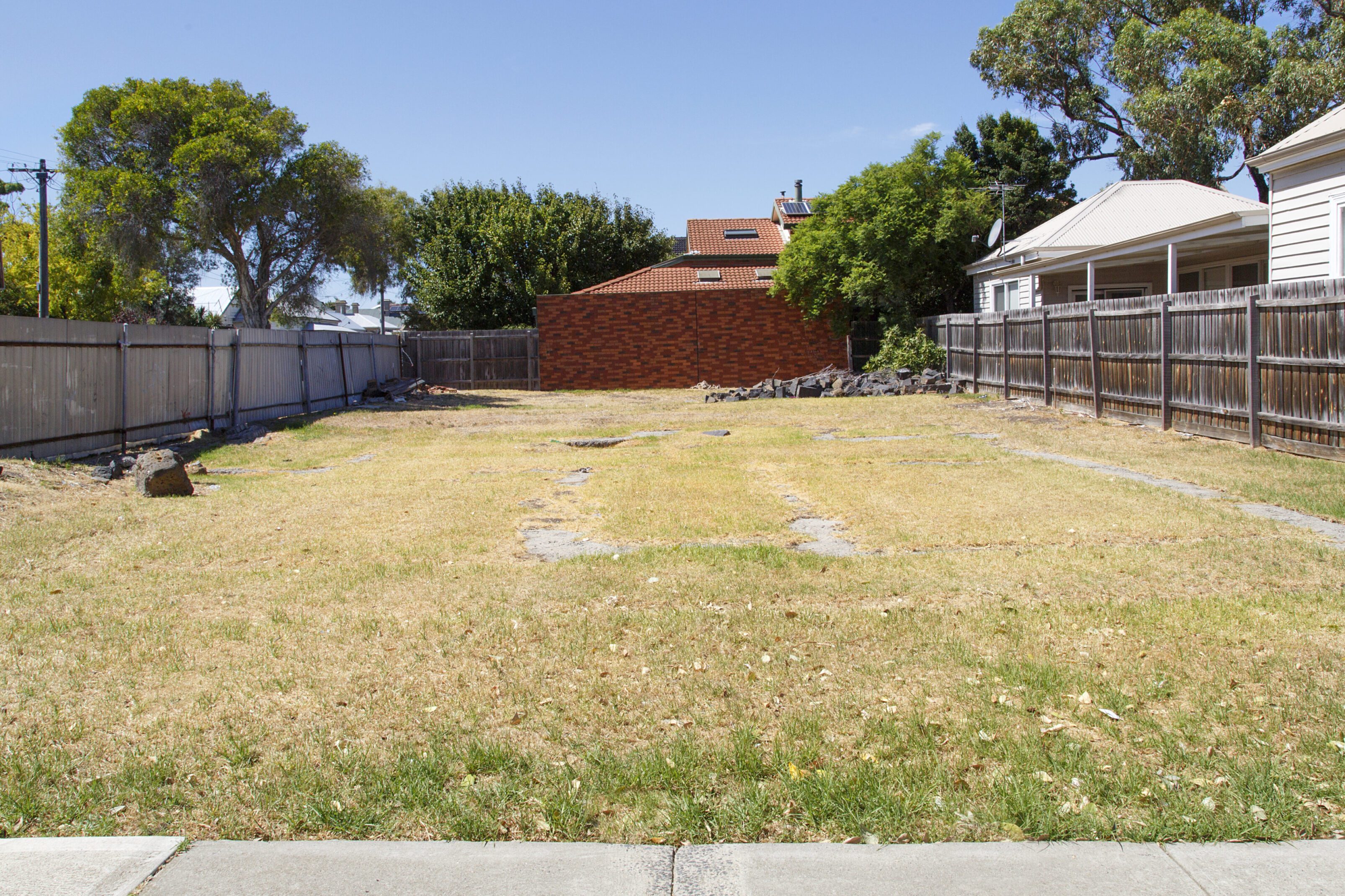 A spacious grassy backyard with trees and a brick wall.