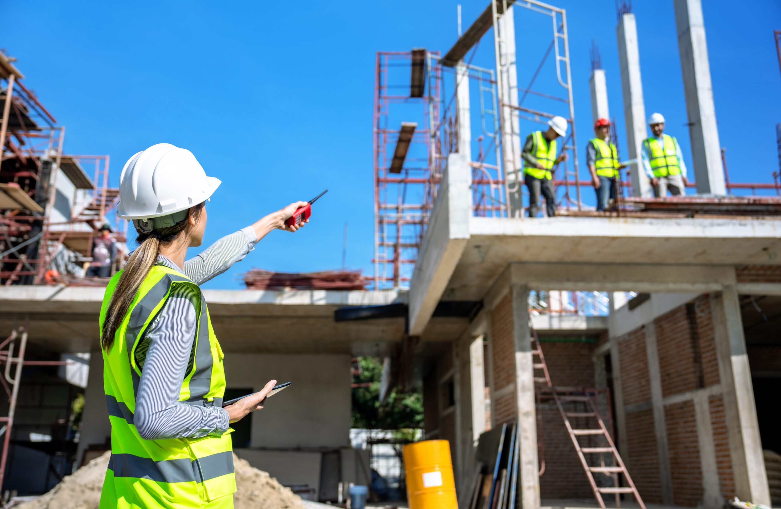 Construction workers inspect a building site under clear blue sky.