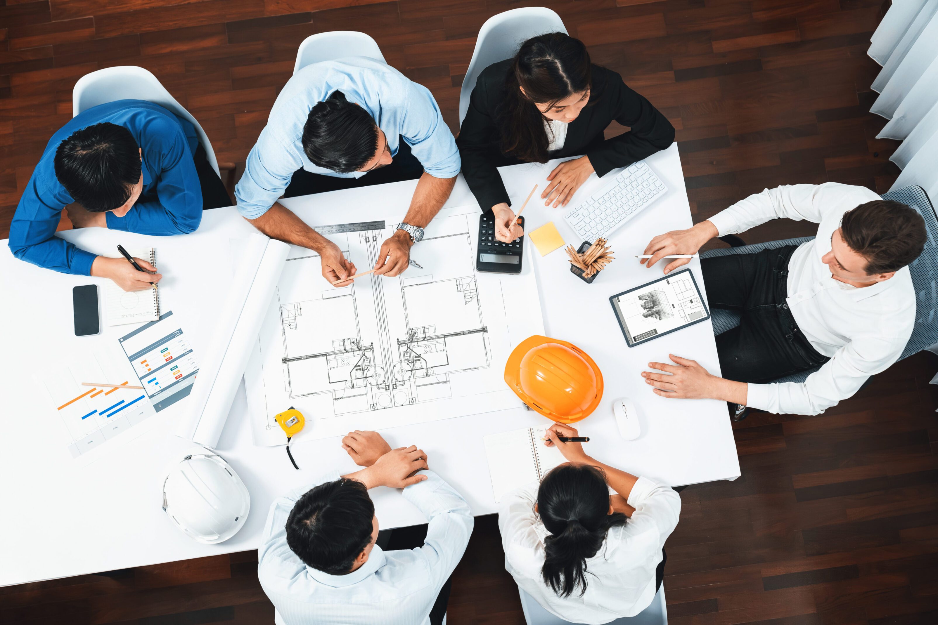 Team collaborating over architectural plans and digital devices in a meeting.