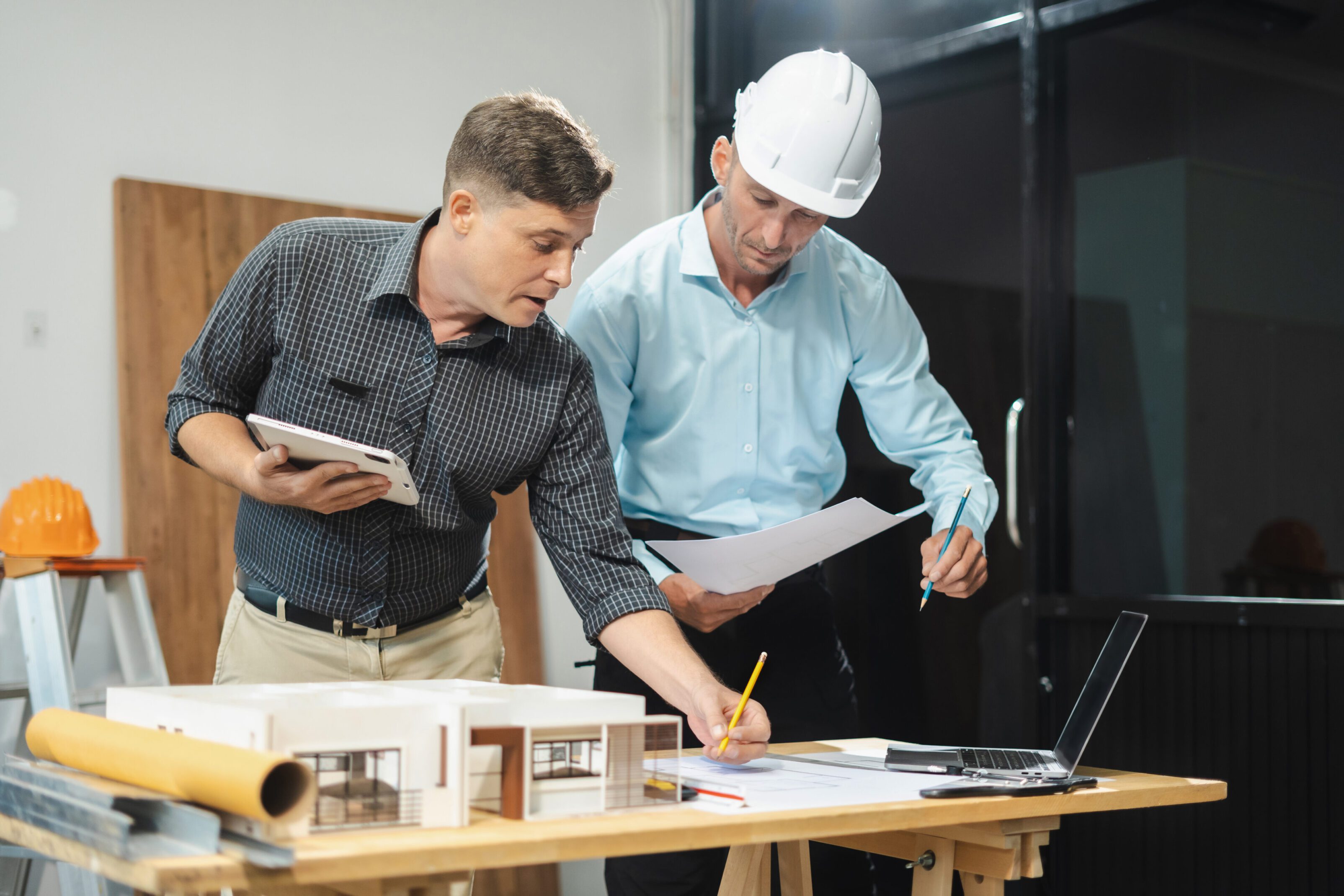 Two men reviewing architectural plans at a workspace.