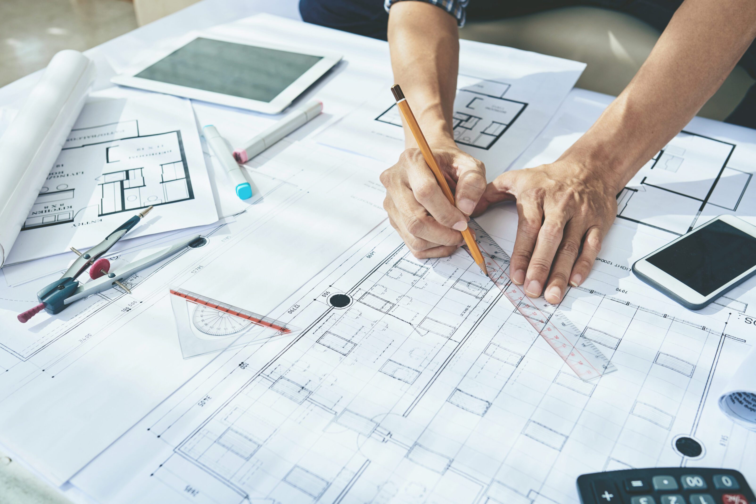 Architect working on building blueprints with drawing tools.