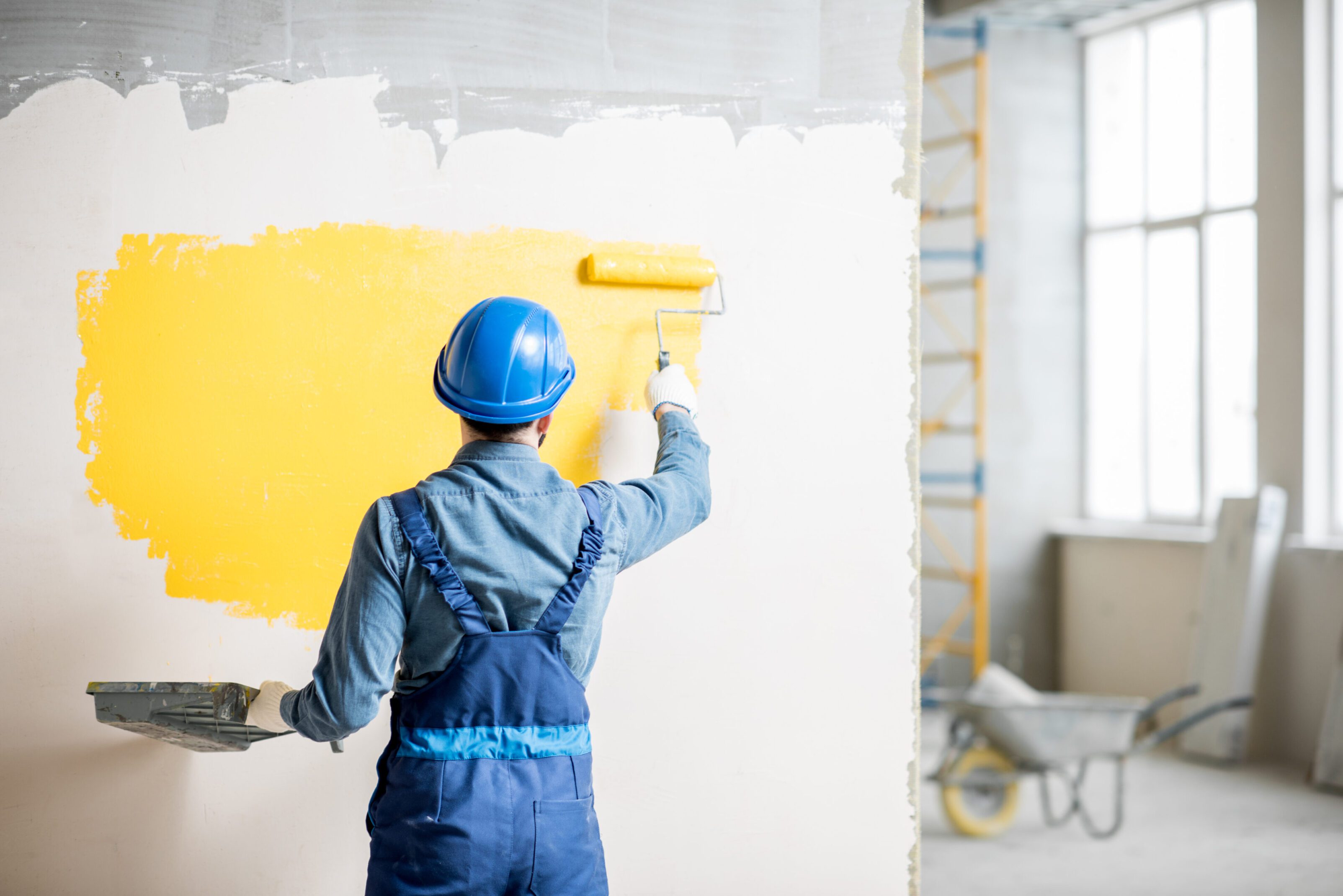 Worker painting wall yellow with roller in construction site.