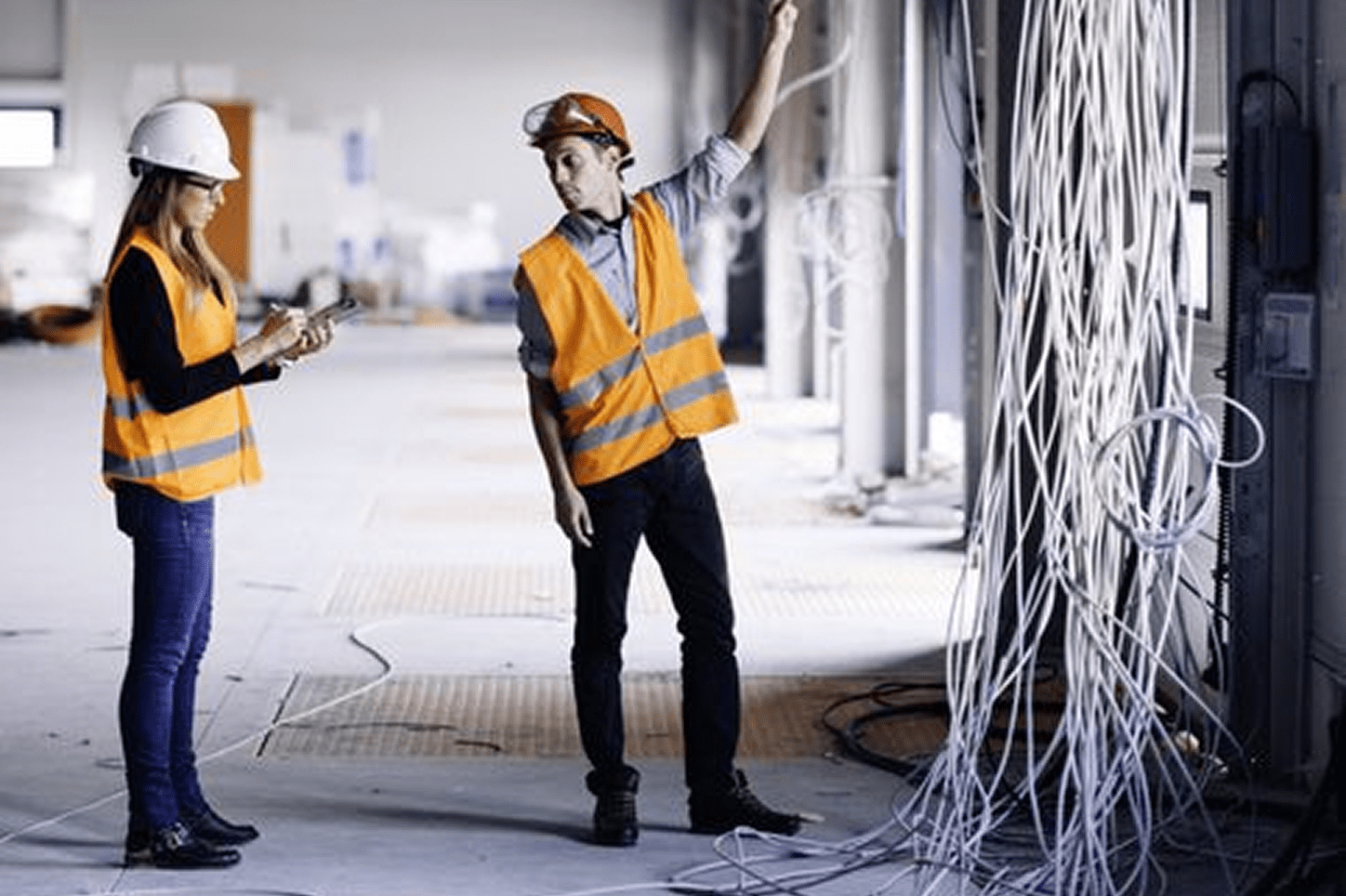 Construction worker in safety gear inspecting hanging cables.