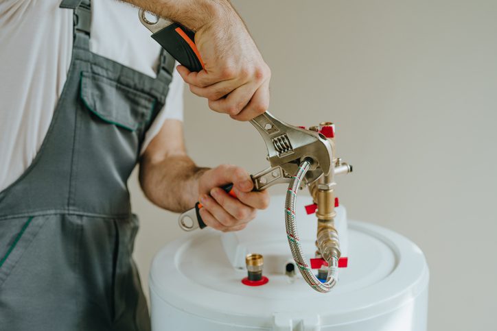 Technician repairing a water heater with tools.