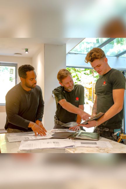 Three men collaborating over architectural plans in a bright workspace.