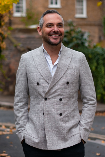 Man in a stylish double-breasted gray blazer smiling outdoors.