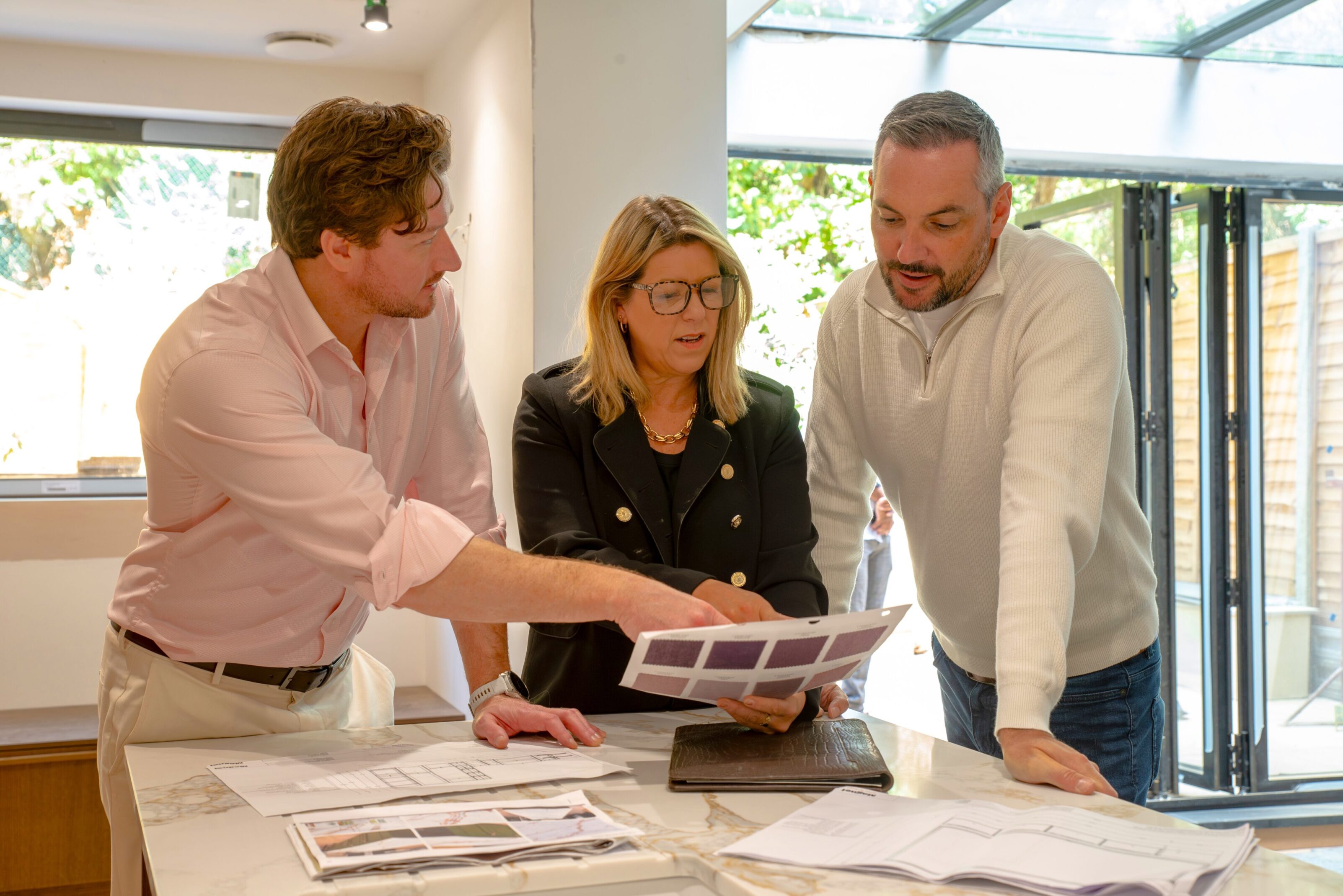 Three colleagues discussing documents around a table in a bright office.